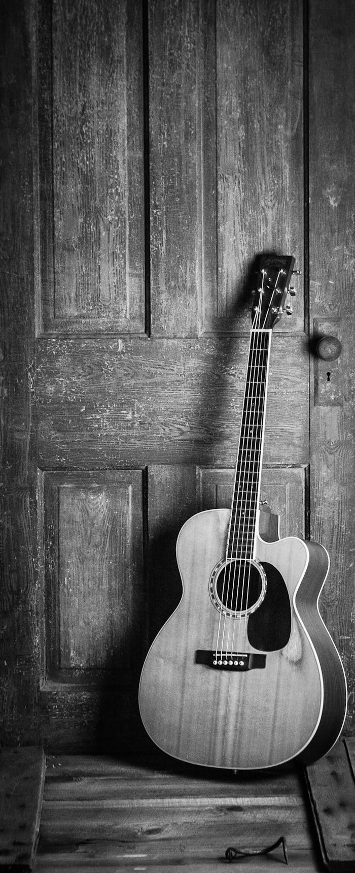 A classic acoustic guitar leaning against a rustic wooden door in a black and white vintage style.